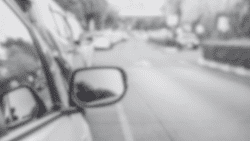 Blurred black and white image of a car on a street.